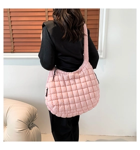 Detailed view of pink quilted puffer shoulder bag with soft padded strap worn by a model