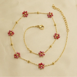 Macro view of gold chain necklace with red beaded flower charms on beige fabric