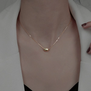 Gros plan d'un collier ras du cou en acier inoxydable avec pendentif haricot doré