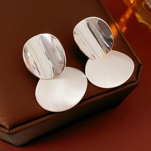 Close-up of silver oval earrings with brushed metal texture on a dark box