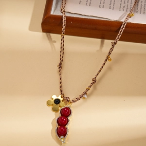 Détail d'un collier tressé avec un pendentif cosse de pois rouge et une fleur dorée