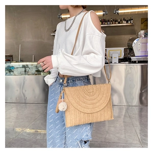 Straw envelope bag with shoulder strap and white pompom detail in a cafe setting