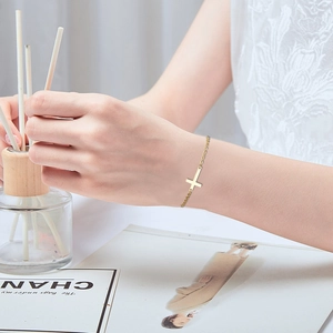 Detail shot of a minimalist gold cross bracelet worn by a model with a soft background