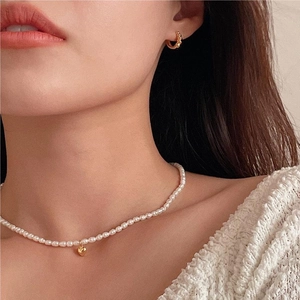 Close-up of pearl necklace with gold heart pendant and beaded gold hoop earrings on model