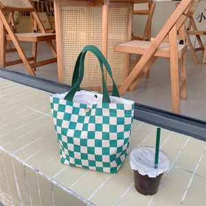 Detail of green checkerboard corduroy tote bag with snap closure on a cafe table