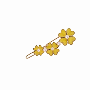 Detail of golden alloy hair clip with yellow clovers and white pearls on white backdrop