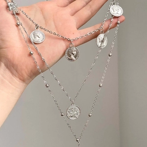 Detail view of silver multi-layered necklace with vintage coin pendants held in hand