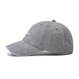 Detail of white cursive embroidery on washed grey cotton baseball cap with vintage texture
