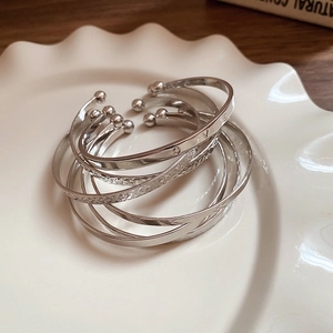 Close-up of stacked silver metal bangles with V-engraving and woven texture on a plate