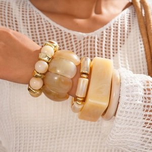 Close-up of bohemian resin bangles and gold beads worn with white crochet lace clothing