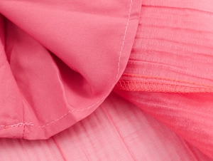 Close-up of pink pleated chiffon fabric showing fine horizontal texture and neat stitching