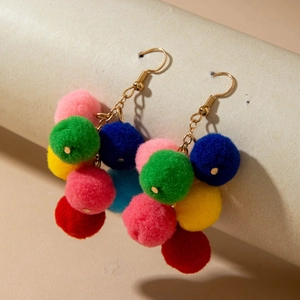 Detail of colorful fuzzy pom-pom drop earrings with golden chains on a textured display