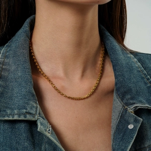Dettaglio di una collana in acciaio al titanio dorato su una modella in giacca di jeans