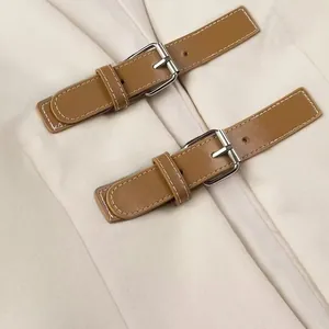 Close-up of brown leather straps with silver buckles on soft cream winter coat fabric