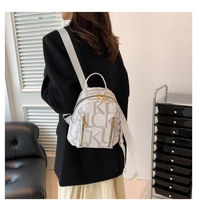 Rear view of model wearing white backpack with letter pattern and golden zippers