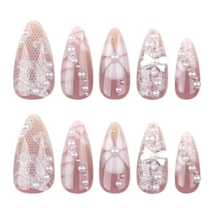 Faux ongles amande courts avec pétales 3D blancs, perles et nœud sur une base rose nude