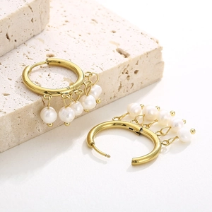 Close-up of gold hollow hoop earrings with five white pearls on stone pedestal