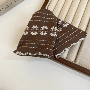 Close-up of brown fabric hair tie with white floral embroidery and ethnic patterns