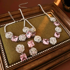 Elegant jewelry set with camellia floral design and pink square crystals on green fabric