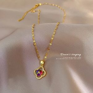 Elegant gold titanium steel clover necklace with a sparkling gemstone on silk fabric