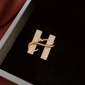 Broche luxueuse en forme de H dorée avec zircons brillants dans un écrin noir élégant