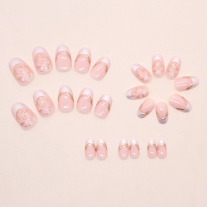 Detail of nude pink press-on nails featuring golden floral relief and French white tips