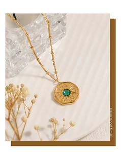 Detail of gold sunburst necklace with green gemstone on a white ceramic plate