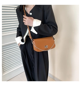 Detail of a brown leather crossbody bag with silver chain and metal clasp worn by a model