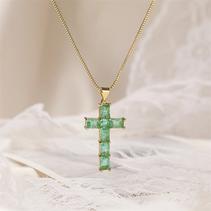 Close-up of golden cross pendant with square-cut green zircon on white lace background