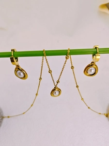 Detail view of pearl drop necklace and hoop earrings set on a golden chain with beads