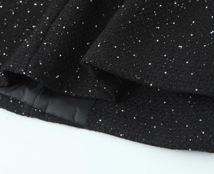 Detailed macro view of black tweed fabric featuring silver sequins and textured weaving