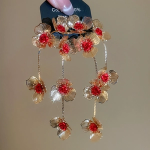 Detail of gold flower tassel earrings with red gemstone inlay and brushed metal texture