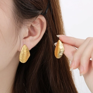 Detailed close-up of golden leaf-shaped earrings with irregular brushed metal texture