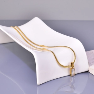 Detail of a gold snake chain necklace with a clear rectangular zircon pendant on a white stand
