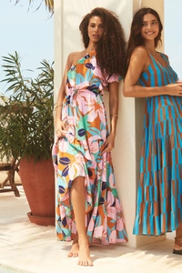 Dettaglio di maxi abiti a fiori monospalla e a righe in un ambiente da resort mediterraneo