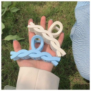 Detail of light blue and beige matte twist shark hair clips held against natural grass
