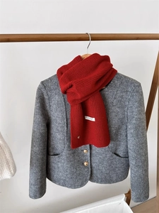 Dettaglio di sciarpa in lana rossa a maglia e cappotto di tweed grigio con bottoni