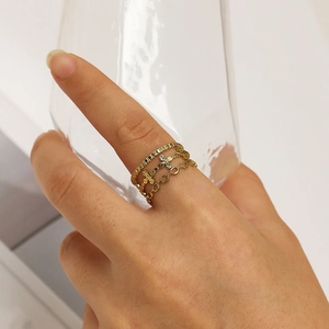 Close-up of three layered gold rings with cross and chain designs on a model hand