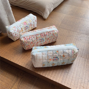 Close-up of quilted floral pencil cases in pink, orange, and blue on a wooden table