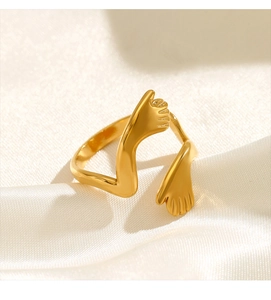 Detail of gold hugging hands ring showing polished texture on white satin background