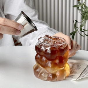 Irregular bubble glass cup for iced coffee with ice cubes and liquid being poured