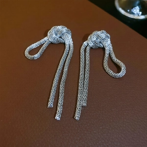 Macro shot of silver mesh knotted fringe earrings on brown textured leather background