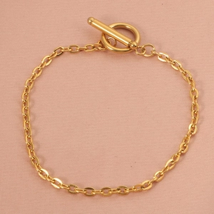 Close-up of golden geometric chain necklace with OT toggle clasp on soft pink fabric