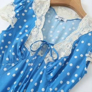 Detailed view of blue polka dot dress neckline with white lace trim on wooden hanger