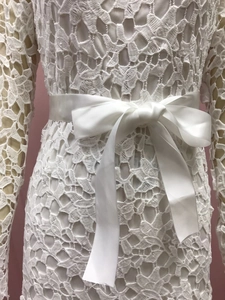 Close-up of white lace dress featuring a delicate satin bow belt on the waistline