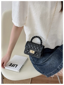 Detail of black quilted PVC jelly bag with beaded handle and golden chain strap