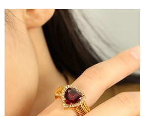Detail of a gold-tone multi-layered ring featuring a red heart gemstone and crystals
