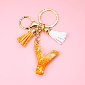 Detail of letter Y resin keychain with gold leaf, orange and white tassels on pink background