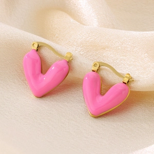 Macro detail of heart-shaped pink enamel earrings with a polished golden metal clasp