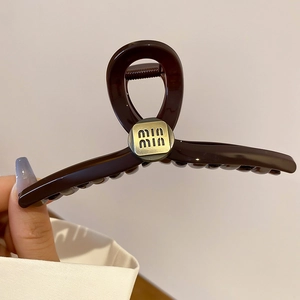 Close-up of a dark brown resin hair claw clip with golden metal logo branding detail
